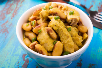 Chicken with white beans in a curry sauce on a blue wooden board