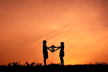 Obraz premium Silhouette children holding money in the sunset.