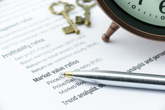 Blue ballpoint pen on a financial ratios analysis check lists with an antique clock and two vintage brass keys. Financial, business and investment analysis concept.
