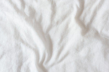 Fototapeta na wymiar Top view of creased / wrinkles on a white unmade / messy bed sheet after waking up in the morning. Bedsheet is not neatly arranged for new guests or customers to sleep in. Abstract texture background