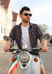 Fototapeta na wymiar fashionable young man riding a vintage scooter in the street