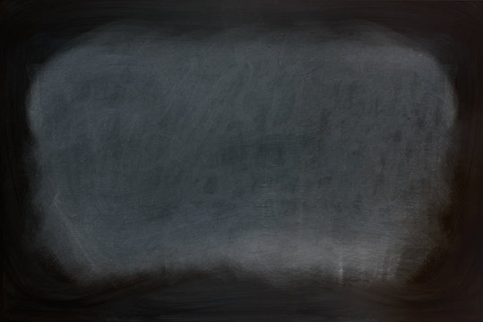 Close up view of a black dirty chalkboard without a wooden frame. Chalk on the blackboard has been rubbed out. Primitive teaching style. Background texture and empty space for further creative design.