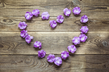 Heart shape made of violet flowers on grunge wooden boards. Plac