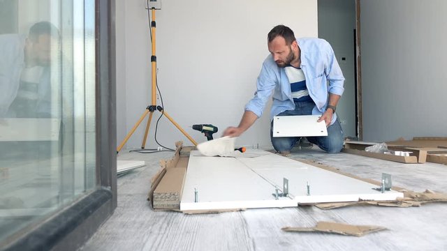 Young man with instruction trying to match pieces of furniture on floor at home
