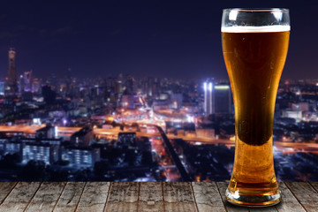 Glass of beer on a wooden City at night background.