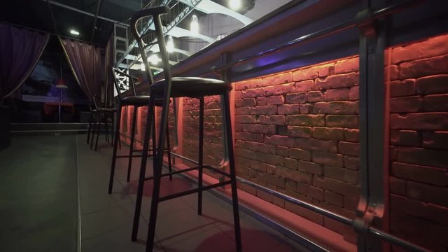 Camera tracks along empty lighted bar counter at night club