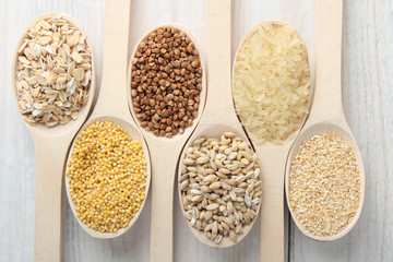 various cereals in wooden spoons on a white wooden table