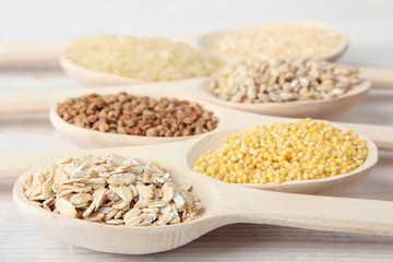 various cereals in wooden spoons on a white wooden table closeup