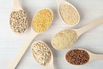 various cereals in wooden spoons on a white wooden table
