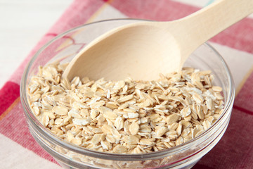 oatmeal in glass bowl with wooden spoon on a napkin on white wooden table