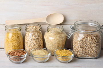 various cereals in glass jars and wooden spoon with glass bowls on a white wooden table