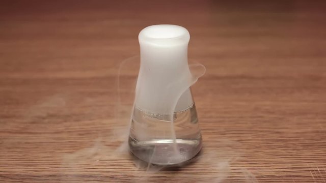 Small conical flask with water and dry ice steaming on wooden table