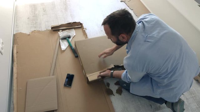 Young man opening box of furniture on floor at home
