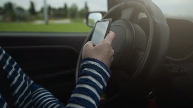 Female driving car on the street and texting sms message on smartphone, using mobile phone in traffic.