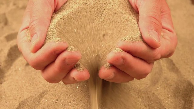 Handful of dry desert sand pouring through male fingers, adult caucasian man holding pile of sandy dust and spilling it onto the ground.