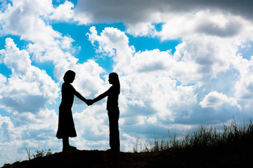 silhouette of two girls facing each other hold hands together