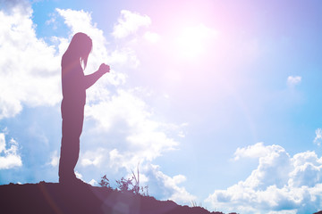 Silhouette of woman praying over beautiful sky background
