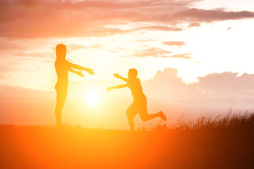 Mother encouraged her son outdoors at sunset, silhouette concept