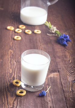 fresh milk in and glass on wooden background.  Milk in glass and wild flowers bouquet over wooden background close up. jug of milk and a bagel.