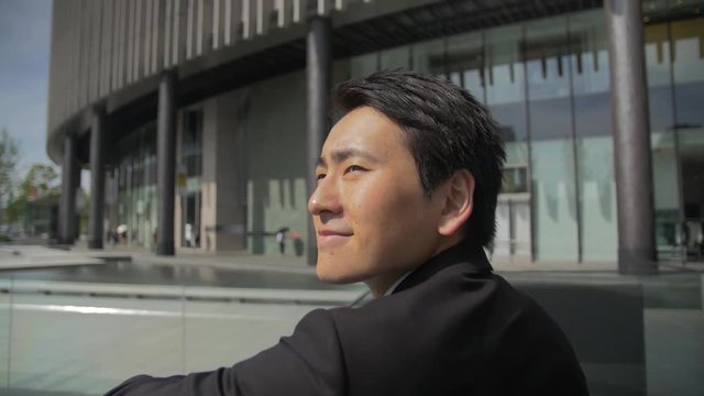 Japanese business man near water relaxing and thinking about success slow motion