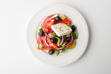 Greek salad in a ceramic plate on a white background