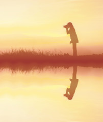 Silhouette woman photographer at sunset with water reflection