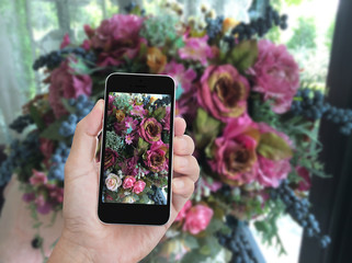 Hand holding mobile phone with flower bouquet background