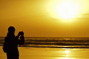 young man taking a picture in front of the sea at dusk