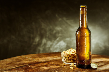 Open bottle of beer near a bowl full of peanuts