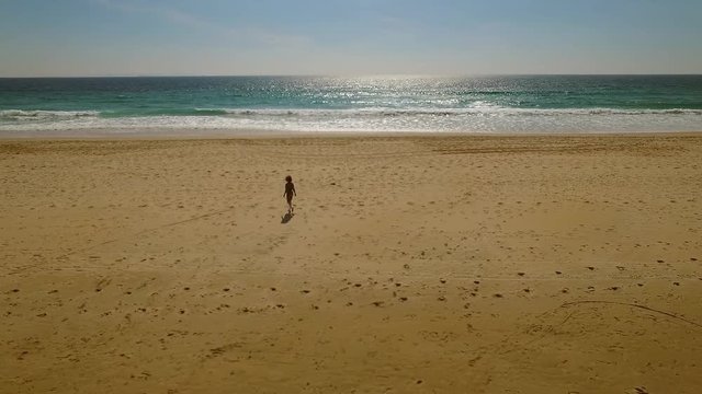 Lone young woman walking on a deserted beach in evening sunlight in a long range view of the vast expanse of sand and ocean