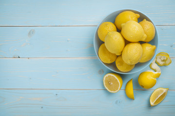 Bowl with fresh lemons on blue wooden background. Top view