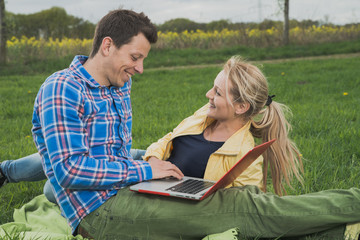 beautiful couple laying at grass and works at laptop