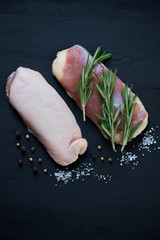 Raw seasoned duck breasts on a black wooden background, top view