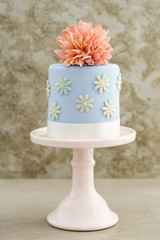 Blue fondant cake with pink sugar peony flower on cake stand