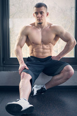 Muscular man sitting on windowsill in gym