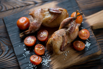 Wooden chopping board with whole baked quails and tomatoes