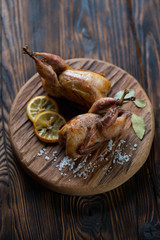 Wooden serving board with baked quails, rustic wooden setting