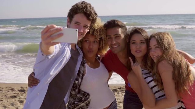 Group of young people makes a selfie on the beach. Five friends take a trip to the beach and take a funny pictures at the sea.