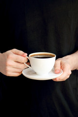 Young man in black holding a white cup  of coffee in his hands