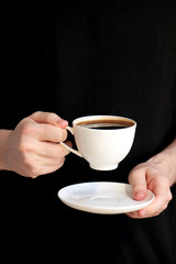 Young man in black holding a white cup  of coffee in his hands