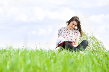 Naklejka na ściany i meble Young smiling woman sitting on meadow and writing something