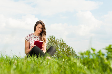 Young beautiful hipster sitting on meadow and reading