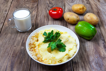 mashed boiled potato with herbs. milk and vegetables on a wooden background