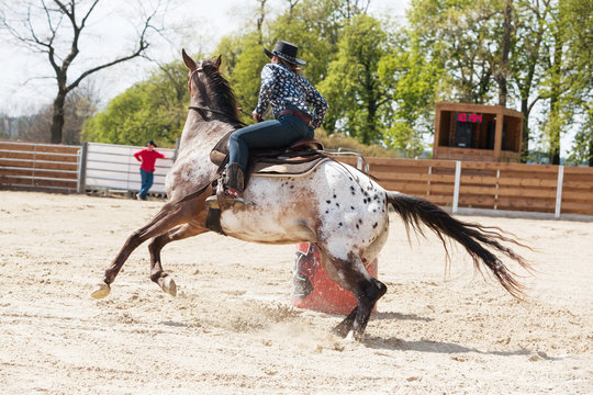 Young cowgirl riding a beautiful paint horse in a barrel racing event at a rodeo.