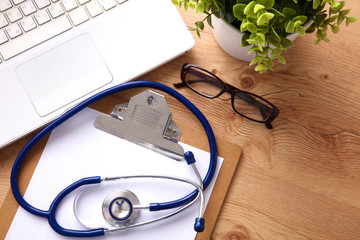 A medical stethoscope near a laptop on a wooden table, on white