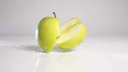Whole green apple falling down and breaking on two halves on wet white floor bouncing with explosive splash and spray. Shot with high speed camera in slow motion mode. White background isolated. - Powered by Adobe
