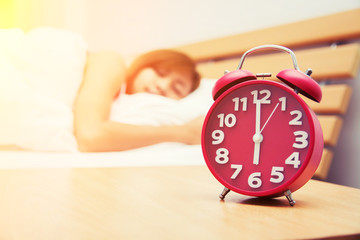 Beautiful young woman sleeping on the bed with red alarm clock i