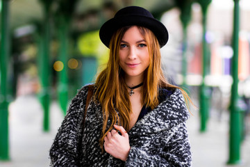 young beautiful girl in a hat and a short dress and jacket on a background of green poles
