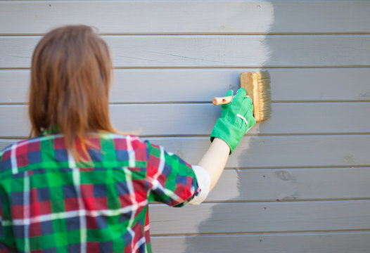 Woman applying protective varnish or paint on wooden house tongue and groove cladding elevation wall. House improvement diy concept.