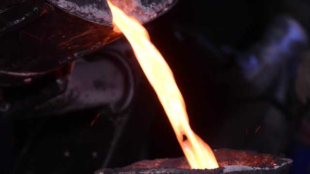 Steel worker in protective clothing raking furnace in an industrial foundry